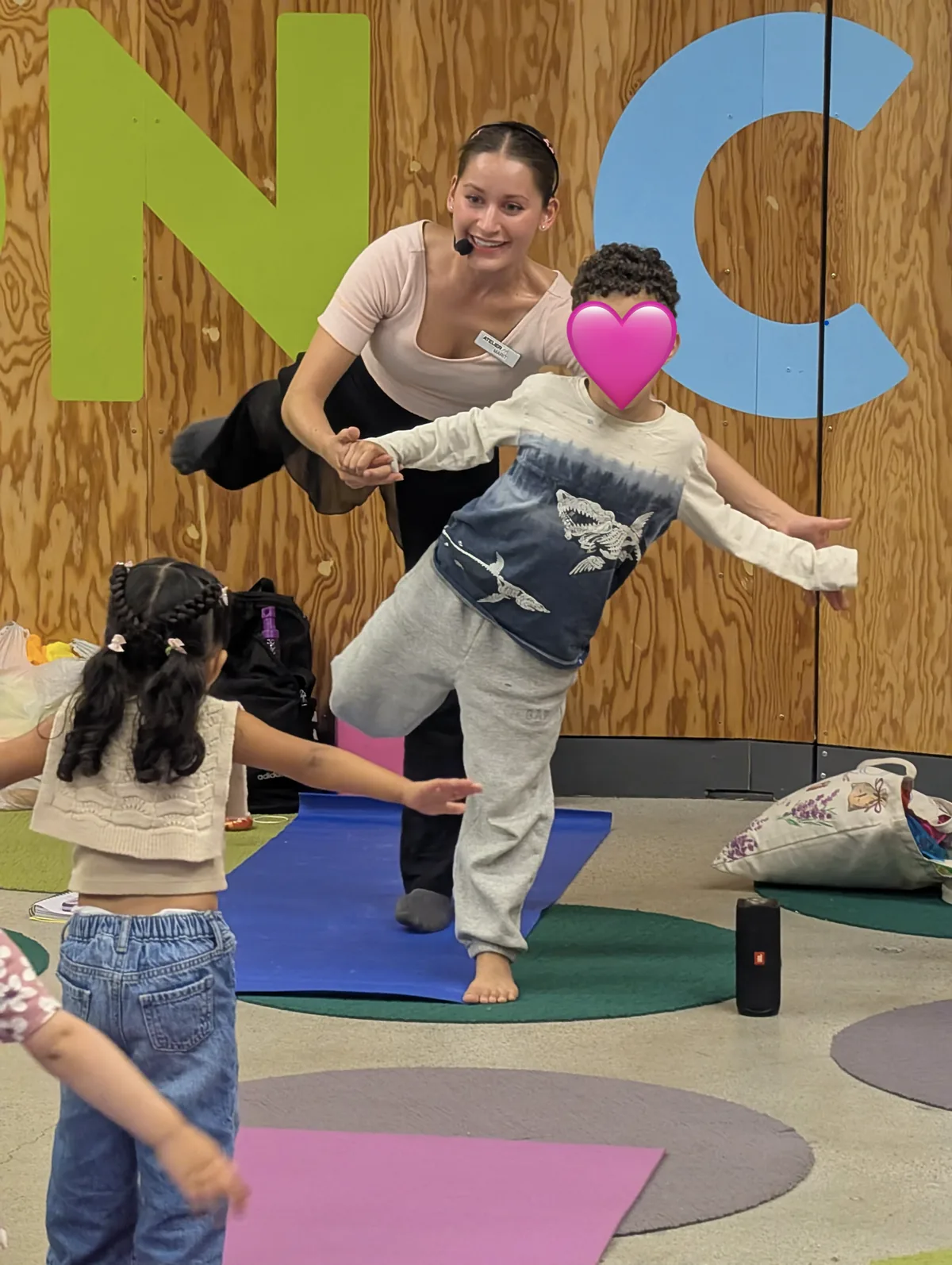 Marit supporting a child balancing on one leg during a group movement activity.